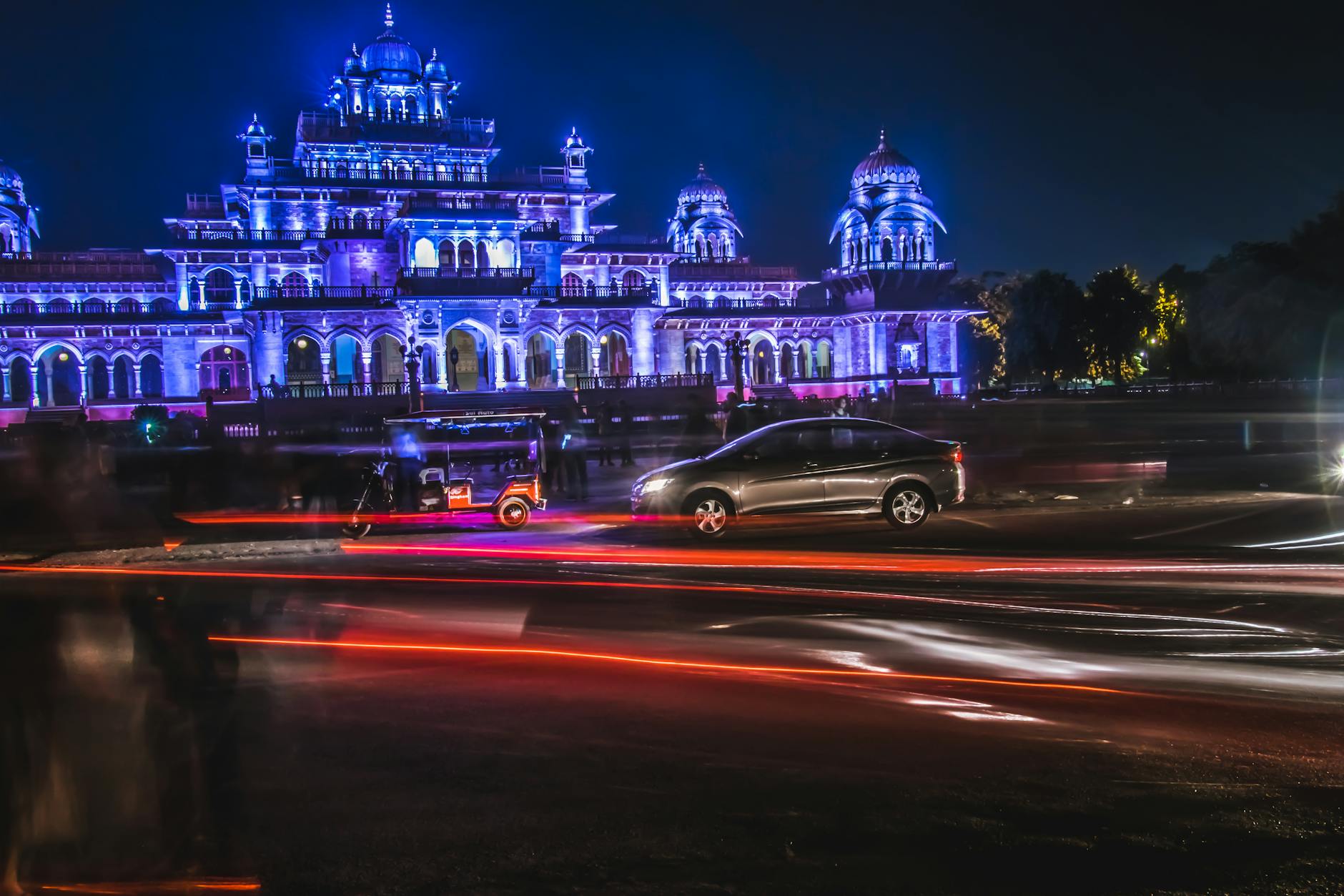 grey sedan and red auto rickshaw in front of purple mansion